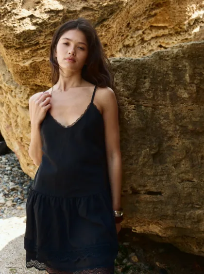 Young woman in a black lace-trim dress posing against a rocky wall outdoors.