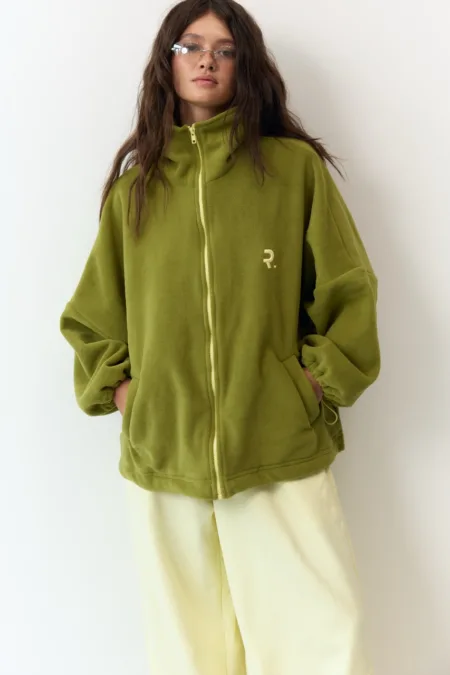 Укорочене пальто сіре oversize із вовни - Person wearing an oversized olive green zip-up fleece with front pockets, standing against a white backdrop.