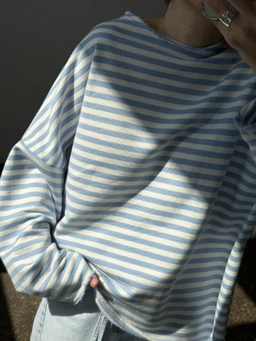 Person wearing a blue and white striped long-sleeve sweater with light-wash jeans, touching their face with a silver ring visible on the finger.