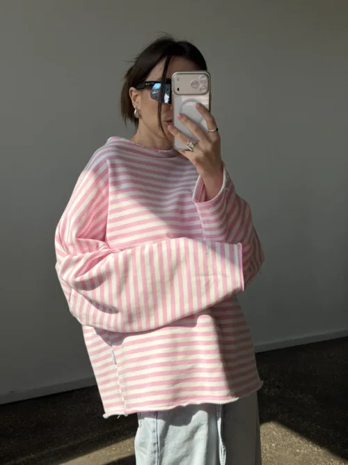 Person in an oversized pink and white striped sweater takes a mirror selfie while wearing dark sunglasses and silver jewelry.