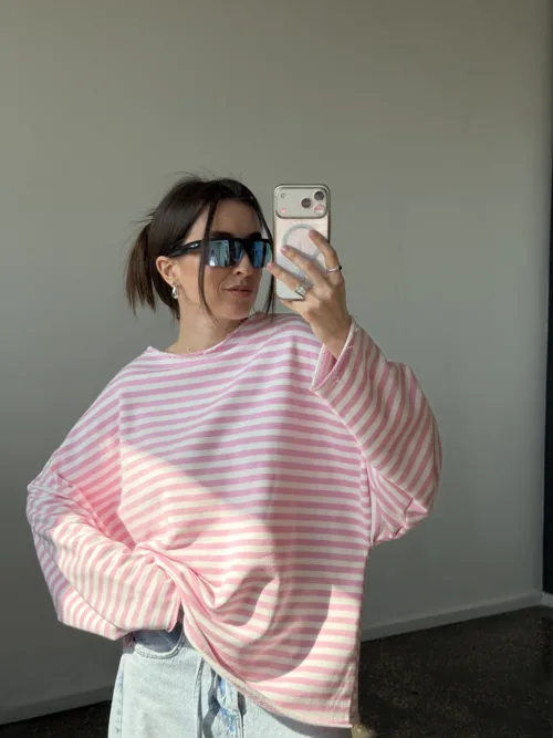 Person posing in a mirror selfie wearing oversized pink and white striped sweater, light jeans, and dark sunglasses, holding a phone.