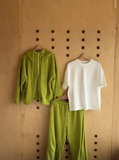 Green hoodie, white T-shirt, and matching green sweatpants hung on a wooden pegboard wall.