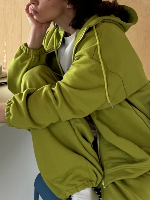 Person wearing a lime-green hoodie rests their head on their hand, seated in a blue chair, side profile visible.