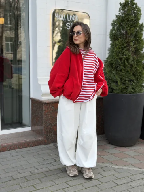 Woman posing outside in a bright red oversized jacket over a red-and-white striped tee, white wide-leg pants, sneakers, and sunglasses.