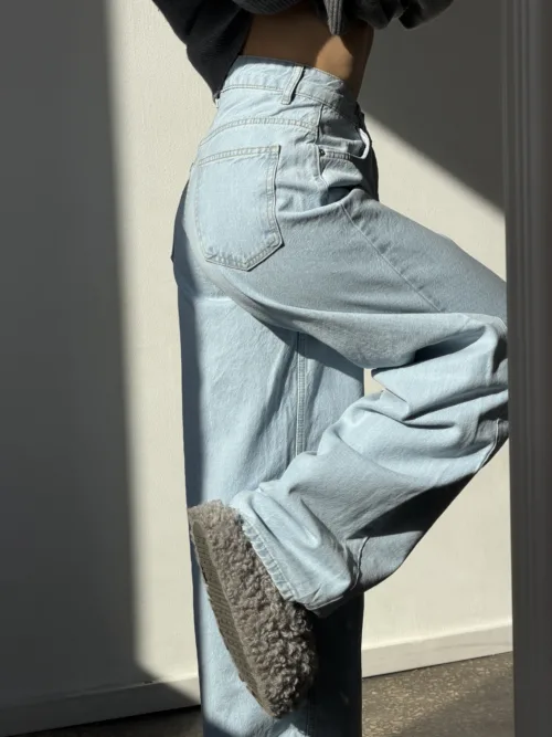 Side view of a person in light-wash denim jeans, with a fluffy gray fleece lining hanging from the pocket area.