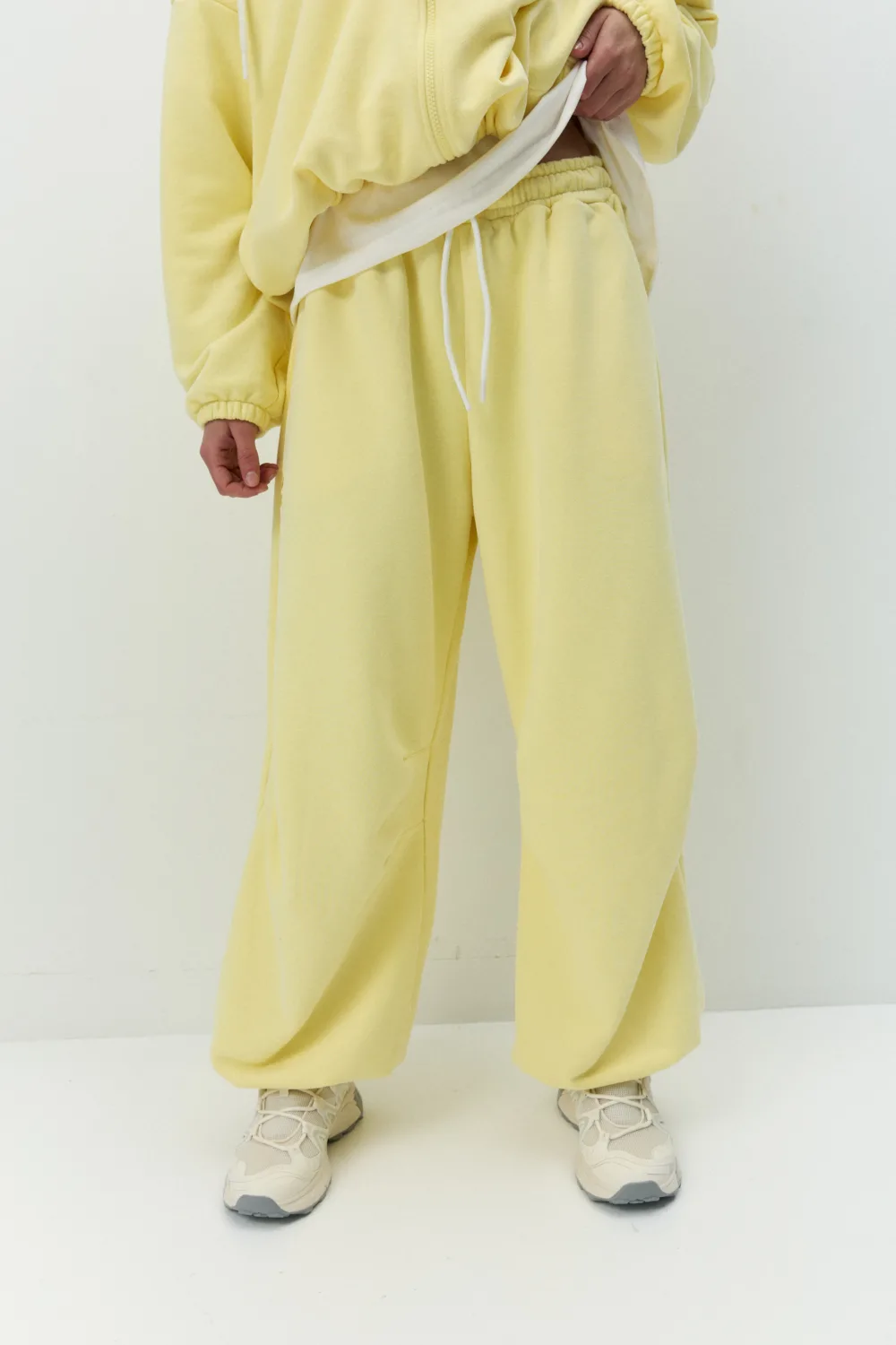 Lower body of person in yellow tracksuit with elastic waistband and white drawstrings, standing on a white floor.