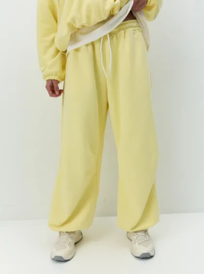 Lower body of person in yellow tracksuit with elastic waistband and white drawstrings, standing on a white floor.