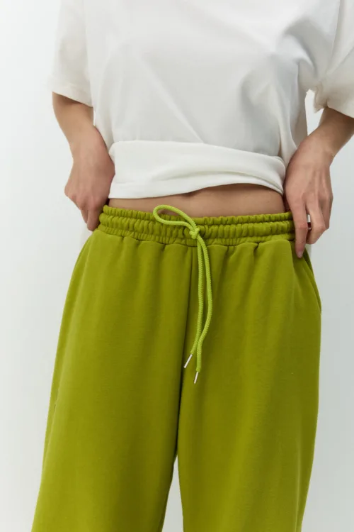 Person wearing a white cropped top and lime green drawstring pants, hands resting at the hips, close-up waist area