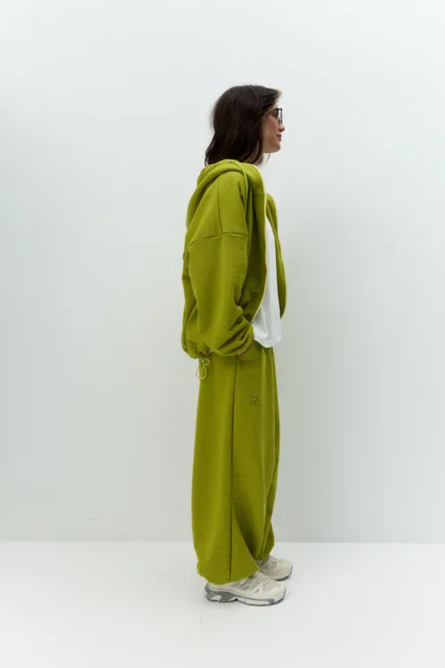Side view of a person wearing a lime-green hoodie and matching pants with white sneakers against a plain light background.
