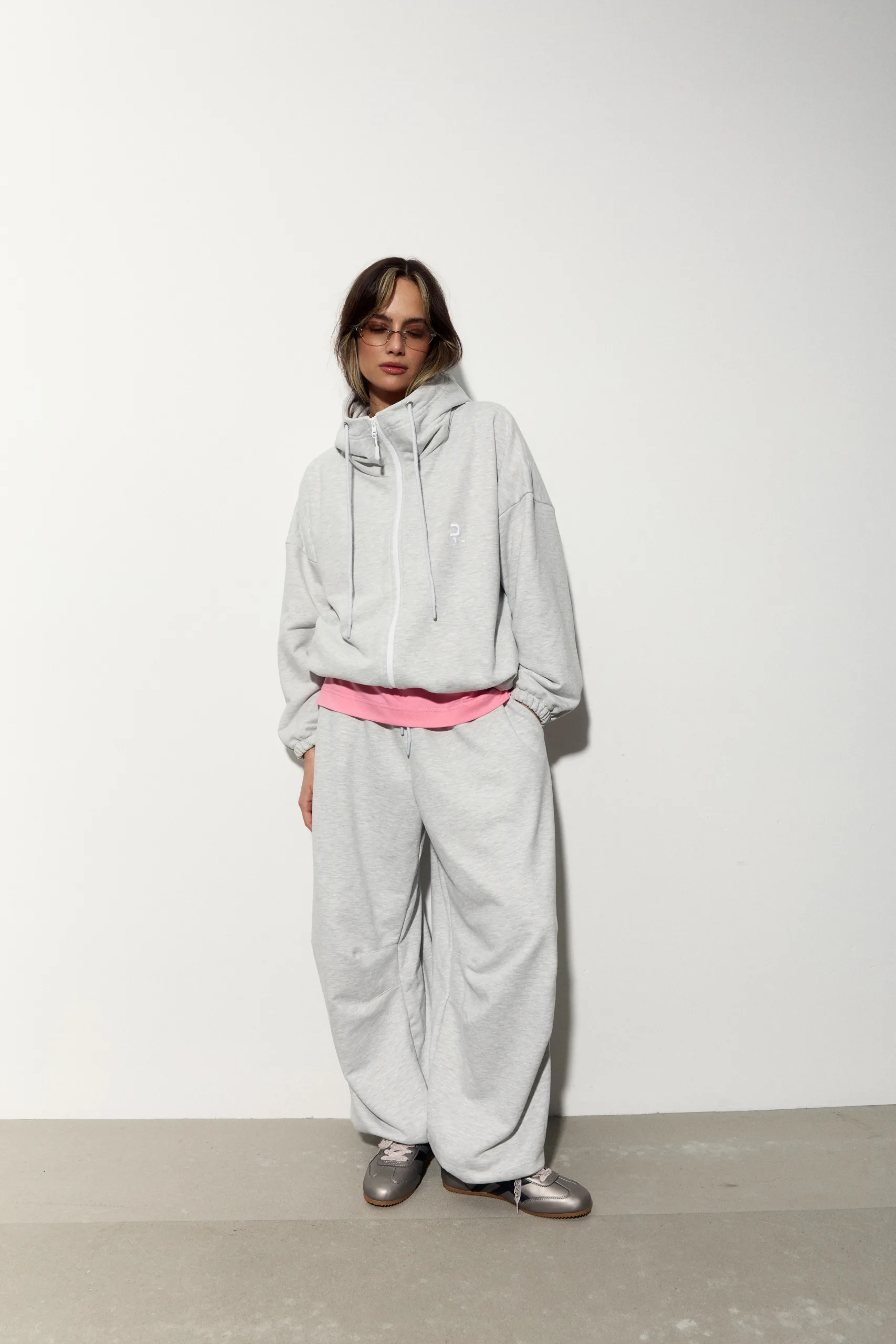 Жіноче oversized худі сірого кольору з футеру діагональ преміум. Вільний силует, блискавка та м’яка фактура для casual образів. - 1C7A1066_Original Худі жіноче oversized сіре на блискавці без утеплення - Person in oversized light gray hoodie and sweatpants with a pink waistband, standing against a white wall.
