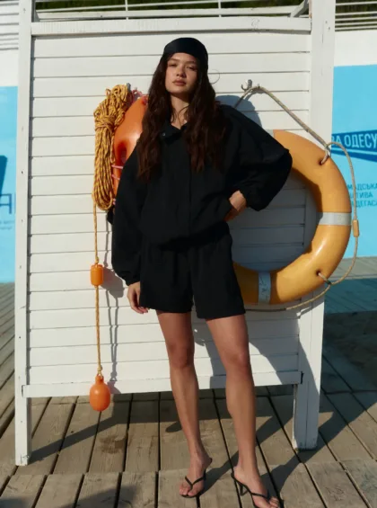 Woman in a black outfit standing on a wooden dock beside a life preserver and coiled rope.