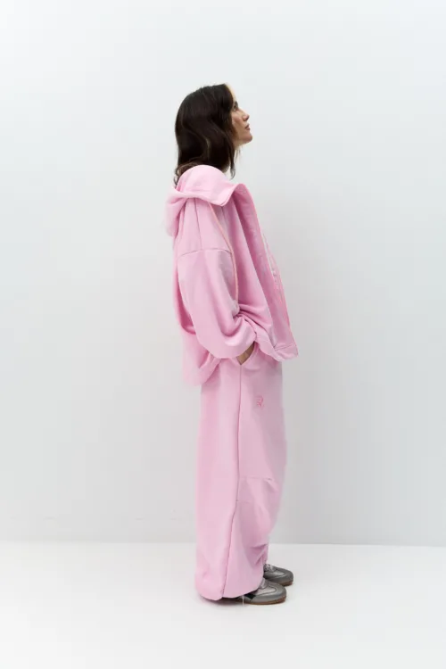 Side view of a person in a pink hoodie and matching sweatpants, standing against a white background.