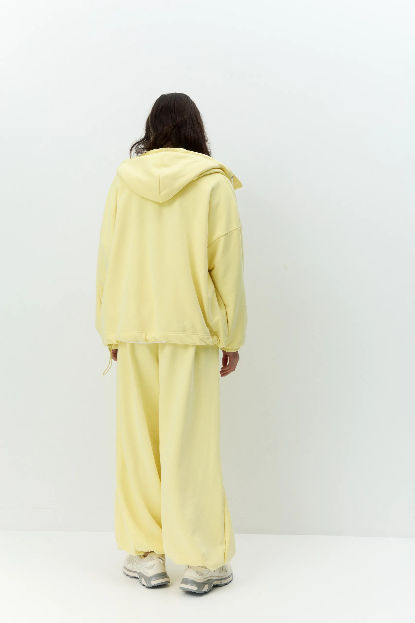 Жіноче oversized худі лимонного кольору з футеру діагональ преміум. Вільний силует, блискавка та м’яка фактура для casual образів. - romanova4434_Original Худі жіноче oversized лимонне на блискавці без утеплення - Person seen from behind wearing a pale yellow hoodie and matching pants, standing against a plain white wall in a studio.