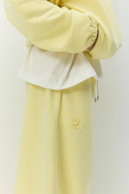 Close-up of a pale yellow tracksuit with an elastic cuff and a white layer, featuring a small embroidered 'P' on the pant leg.