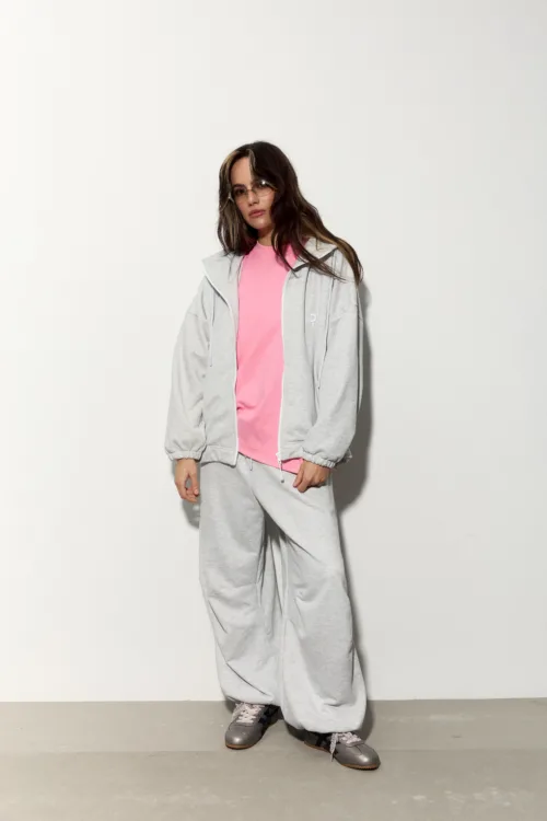 Person modeling casual athleisure: pink t-shirt under a gray zip-up hoodie and matching gray sweatpants, standing against a light background.