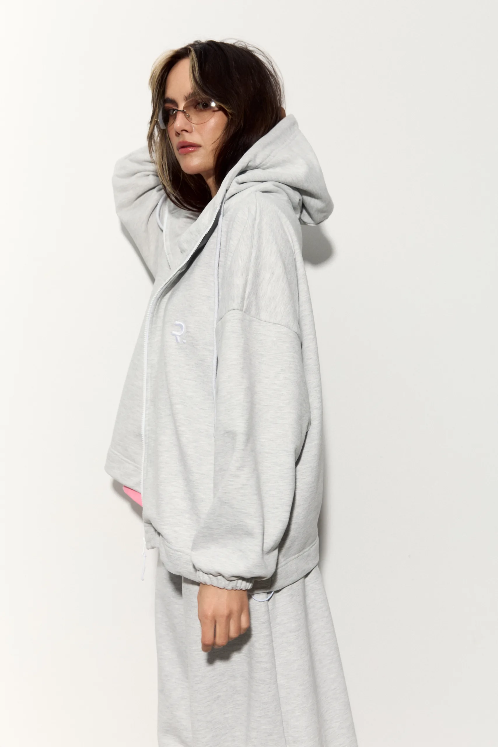 Жіноче oversized худі сірого кольору з футеру діагональ преміум. Вільний силует, блискавка та м’яка фактура для casual образів. - romanova4931_Original Худі жіноче oversized сіре на блискавці без утеплення - Person in a light gray oversized hoodie, shown in profile, wearing tinted sunglasses against a white background.