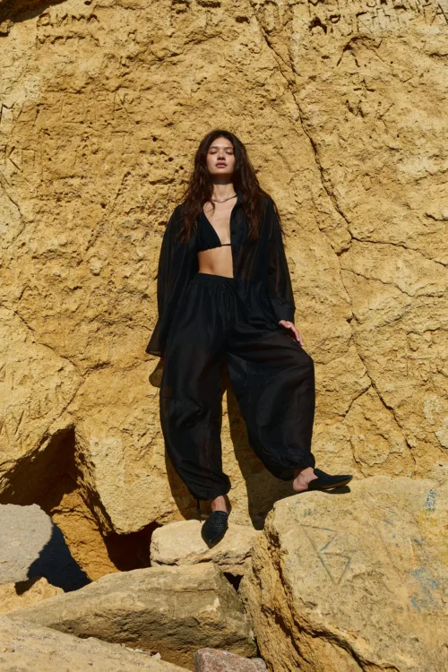 Young woman in a black outfit standing on a sunlit yellow rock cliff.