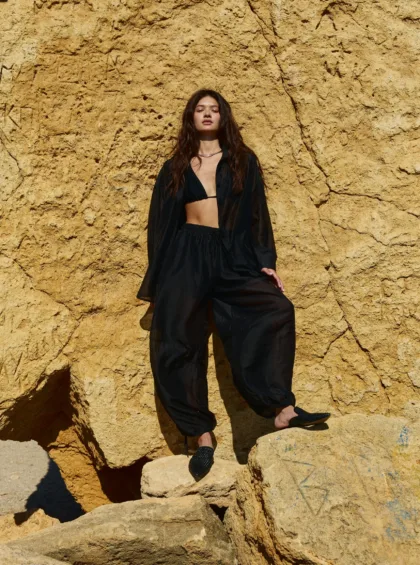 Young woman in a black outfit standing on a sunlit yellow rock cliff.