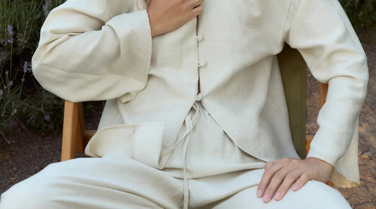 Лляний одяг для стильного літнього гардероба - Person seated outdoors wearing a cream linen suit with a buttoned jacket and tied waist.