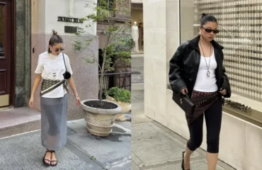 Woman walking on a city sidewalk in a white top, olive wrap belt, gray midi skirt, sandals, and sunglasses.