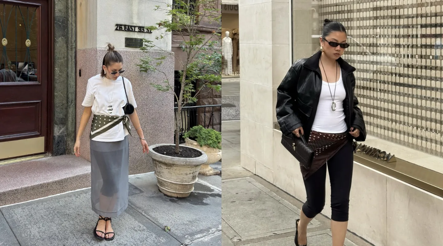 Woman walking on a city sidewalk in a white top, olive wrap belt, gray midi skirt, sandals, and sunglasses.