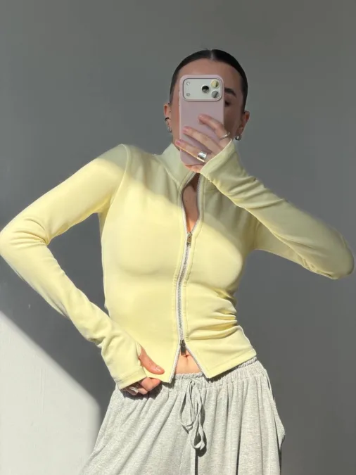 Худі жіноче оверсайз сіре з кишенею бавовна без утеплення - Person taking a mirror selfie, wearing a pale yellow zip-up top and gray drawstring pants, phone obscuring their face.