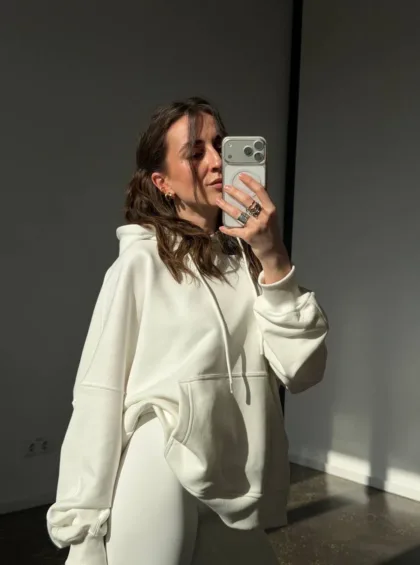 Person wearing a cream oversized hoodie takes a mirror selfie with a smartphone
