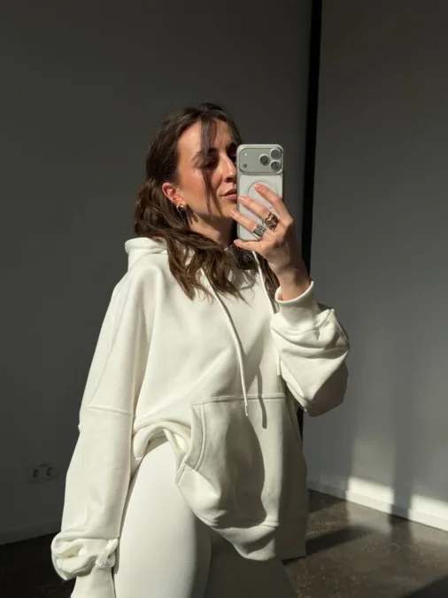 Худі жіноче оверсайз сіре з кишенею бавовна без утеплення - Person wearing a cream oversized hoodie takes a mirror selfie with a smartphone