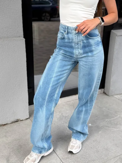 Лонг жіночий у рожеву смужку oversize з бавовни - Person wearing light-wash high-waisted jeans with a white top, standing on a sidewalk outdoors.