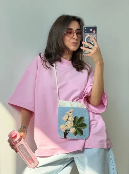 photo_5402427976692996428_y Woman in a loose pink T-shirt and light jeans posing for a selfie with a pastel blue floral crossbody bag; wearing pink sunglasses and holding a pink water bottle.