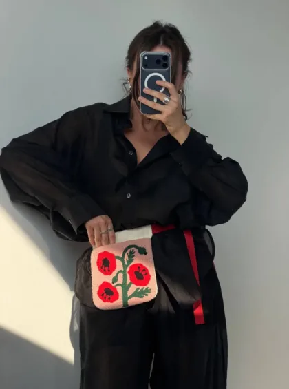 photo_5402427976692996448_y Person in an oversized black shirt taking a mirror selfie with a phone, holding a pink crossbody bag embroidered with red flowers.