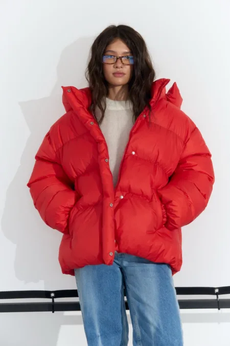 Пуховик чорний жіночий оверсайз екопух до -15°C XS/S M/L - Person wearing a bright red oversized puffer jacket with hands in pockets, standing against a white wall.