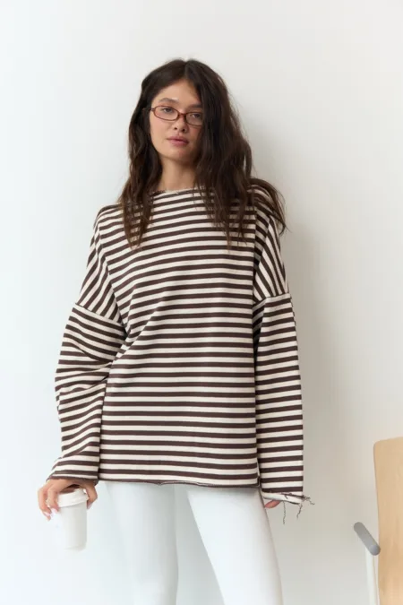 Сорочка жіноча утеплена клітинка кашемір оверсайз one size Romanova - Young woman with brown hair and glasses wearing a brown-and-white striped oversized sweater, holding a white coffee cup against a white wall.