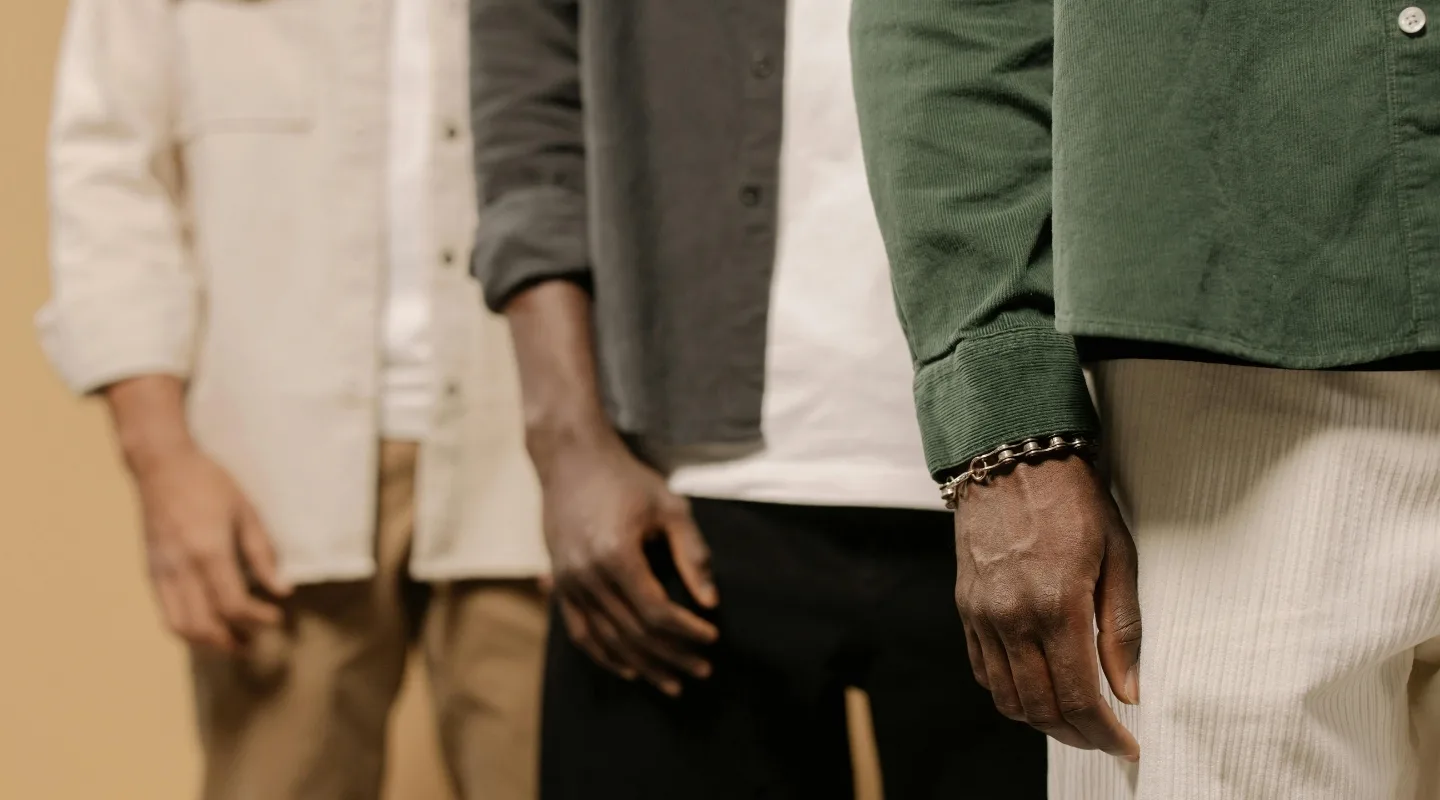 cholovichyy-odyah-na-osin-bazova-kapsula-z-futbolky-khudi-shtaniv-i-shortiv Three people standing side by side, cropped to show their hands and earth-toned outfits.