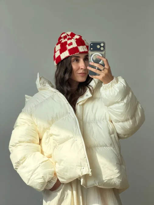Бомбер жіночий флісовий червоний one size полар-фліс - Woman taking a mirror selfie in a cream puffer jacket and a red-and-white checkered knit beanie.