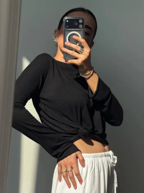 Лонгслів жіночий лимонний приталений напівпрозорий XS/S M/L - Person taking a mirror selfie wearing a black knotted top and white drawstring pants; phone covers face, accessories include rings and bracelets.