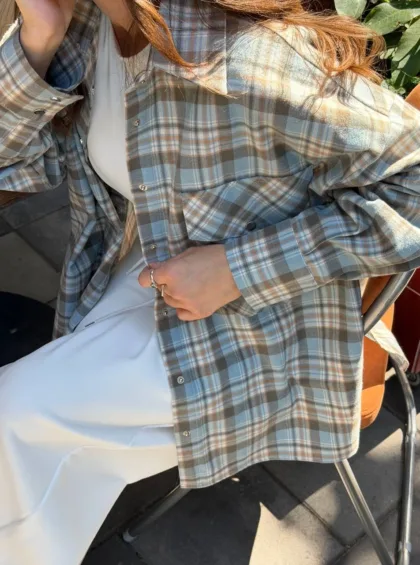 Person wearing a blue-gray plaid shirt over a white dress, seated outdoors on a metal chair.