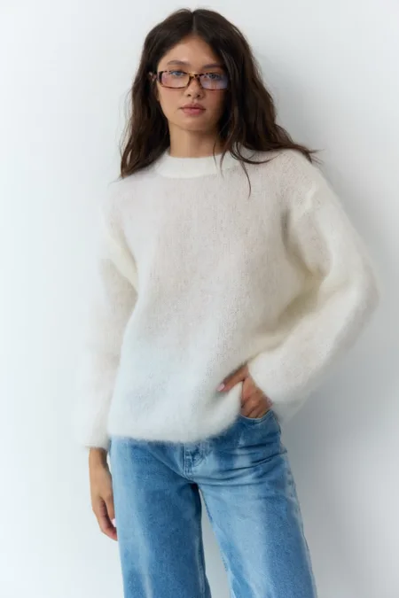 Светр жіночий оливковий бавовняний one size - Woman with dark hair and tortoiseshell glasses wearing a fluffy white knit sweater and light blue jeans, standing against a light wall.