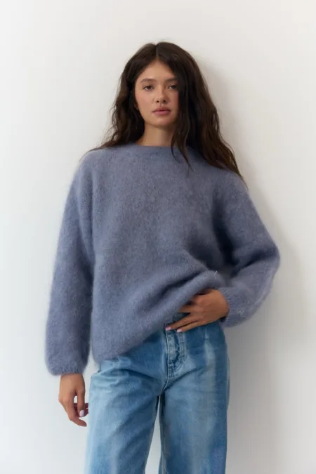 Светр жіночий оливковий бавовняний one size - Woman wearing an oversized fuzzy blue sweater and light-wash jeans, standing against a white wall and looking at the camera.