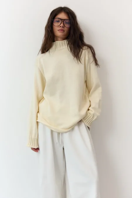 Светр жіночий оливковий бавовняний one size - Woman modeling a cream knit sweater and white wide-leg pants, wearing glasses, standing against a light background.
