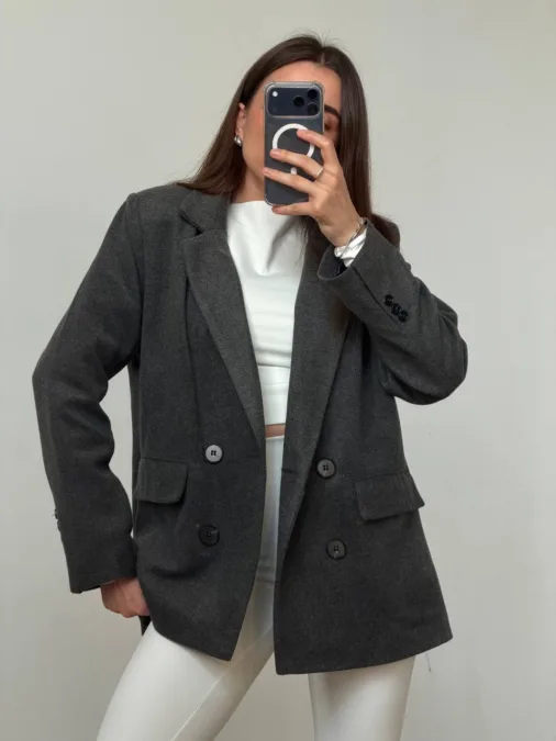 Укорочене пальто сіре oversize із вовни - Person in a dark gray oversized blazer over a white top and white pants, taking a mirror selfie with a smartphone.