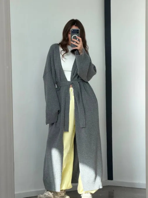 Укорочене пальто сіре oversize із вовни - Person taking a mirror selfie wearing a long gray robe tied at the waist over a white top and pale yellow wide-leg pants with sneakers.
